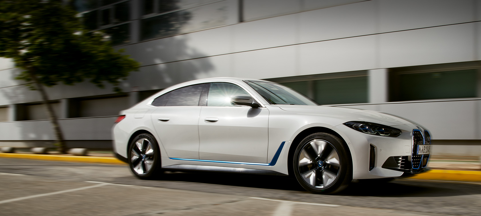 BMW i4 eDrive40 (G26) 2021, pastato fone važiuojančio automobilio trijų ketvirčių vaizdas iš šono BMW i4 eDrive40 (G26) 2021, pastato fone važiuojančio automobilio trijų ketvirčių vaizdas iš šono