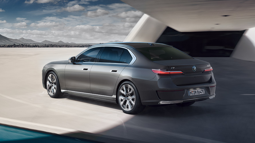 BMW i7 sedanas G70 BMW Individual pilkos metalizuotos Oxid grey spalvos 3/4 vaizdas iš galo pastato fone BMW i7 sedano paketas 3/4 vaizdas iš galo