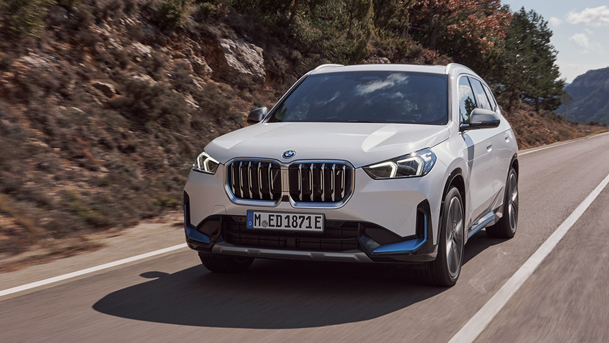 BMW iX1 U11 pirmoji karta keliu važiuojančio automobilio trijų ketvirčių vaizdas iš priekio BMW X serija BMW iX1 U11 pirmoji karta, keliu važiuojančio automobilio trijų ketvirčių vaizdas iš priekio