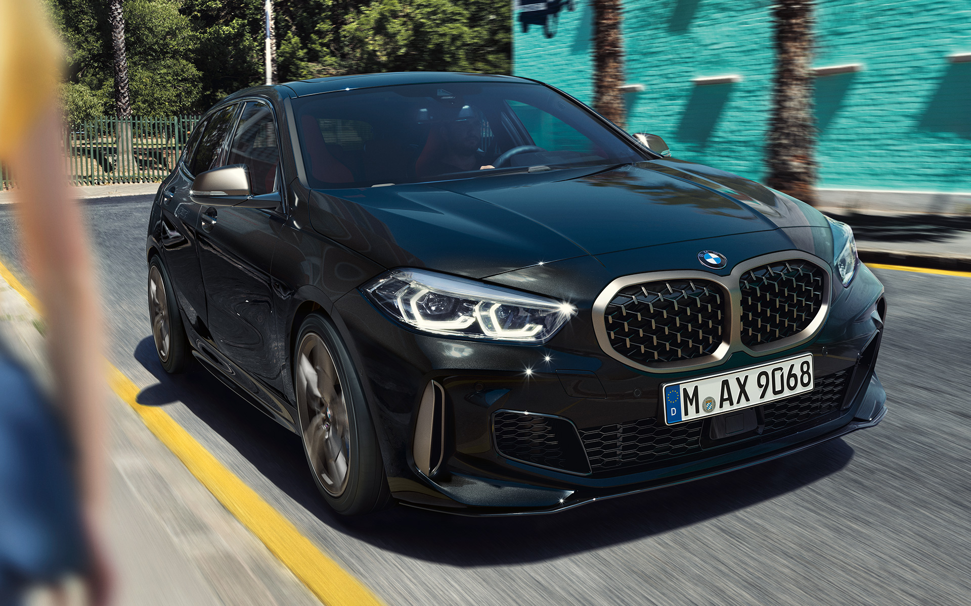 BMW M135i xDrive (F40), juodos metalizuotos Black Sapphire spalvos, važiuojančio automobilio trijų ketvirčių vaizdas iš priekio