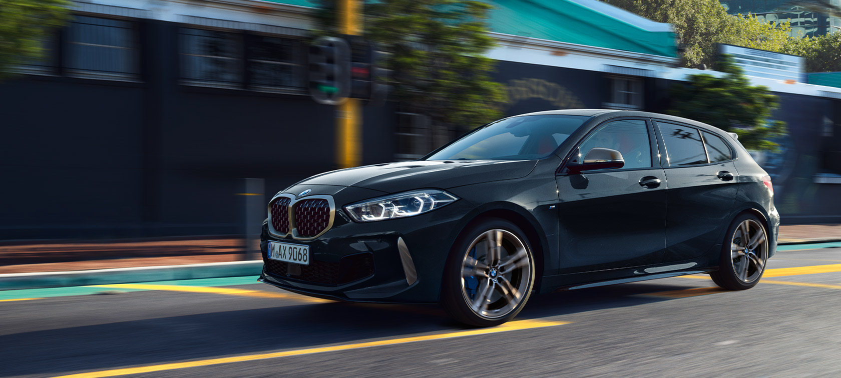 BMW 1 serijos M135i xDrive (F40) juodos metalizuotos Black Sapphire spalvos, miesto fone važiuojančio automobilio vaizdas 