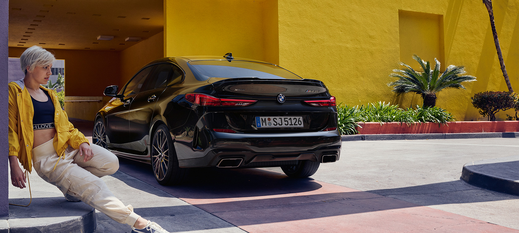 BMW M235i xDrive Gran kupė trijų ketvirčių vaizdas iš galo BMW M235i xDrive Gran kupė Black Sapphire juodo metaliko spalvos F44 trijų ketvirčių vaizdas iš galo su moterimi priešais