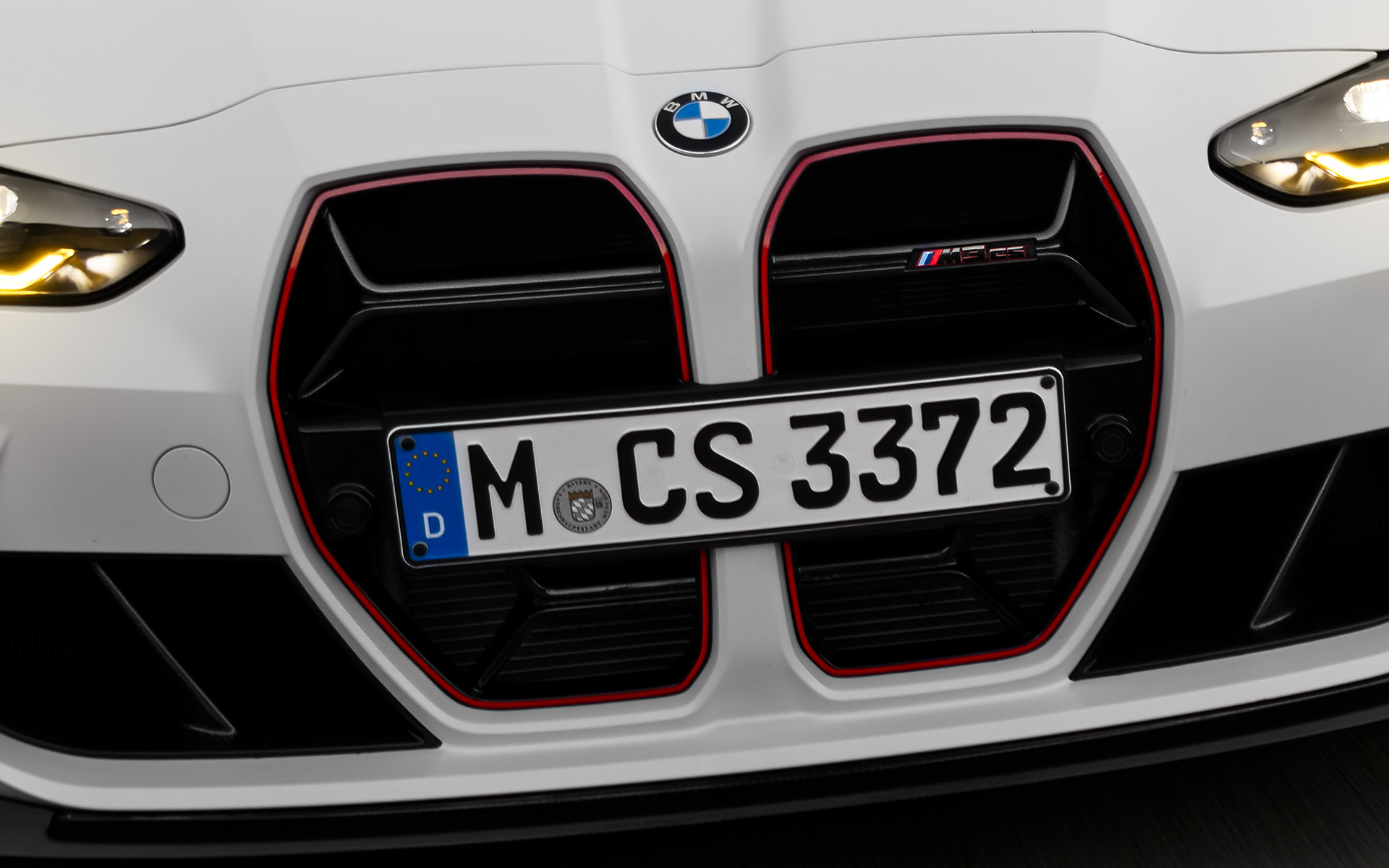 CS juodos spalvos priekinės grotelės su raudona emblema BMW M3 CS G80 BMW M3 CS G80 juodos spalvos priekinės grotelės su raudona emblema, važiuojančio automobilio vaizdas iš priekio