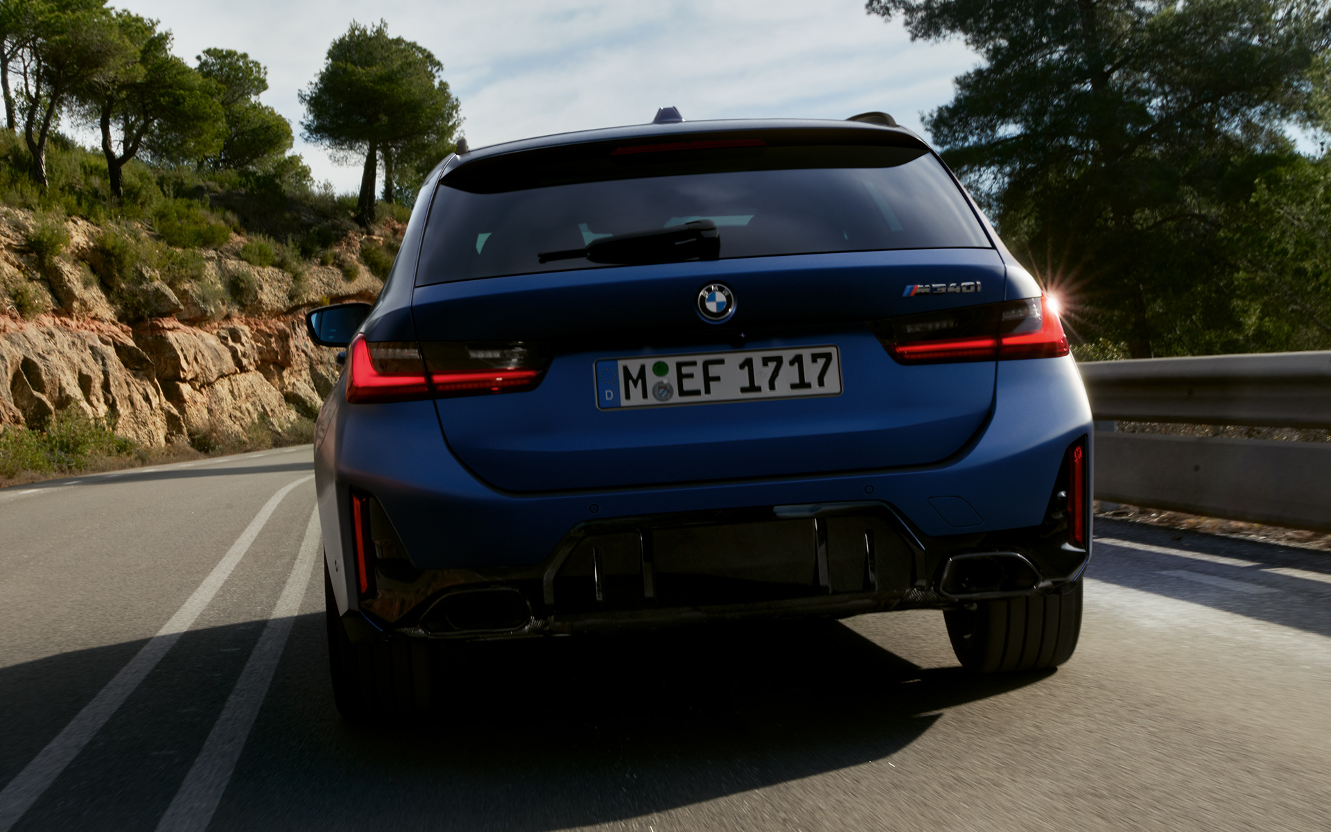 Gatve važiuojančio BMW M340i xDrive Touring G21 vaizdas iš galo Gatve važiuojančio BMW M340i xDrive Touring G21 mėlynos Frozen Tanzanite Blue spalvos vaizdas iš galo