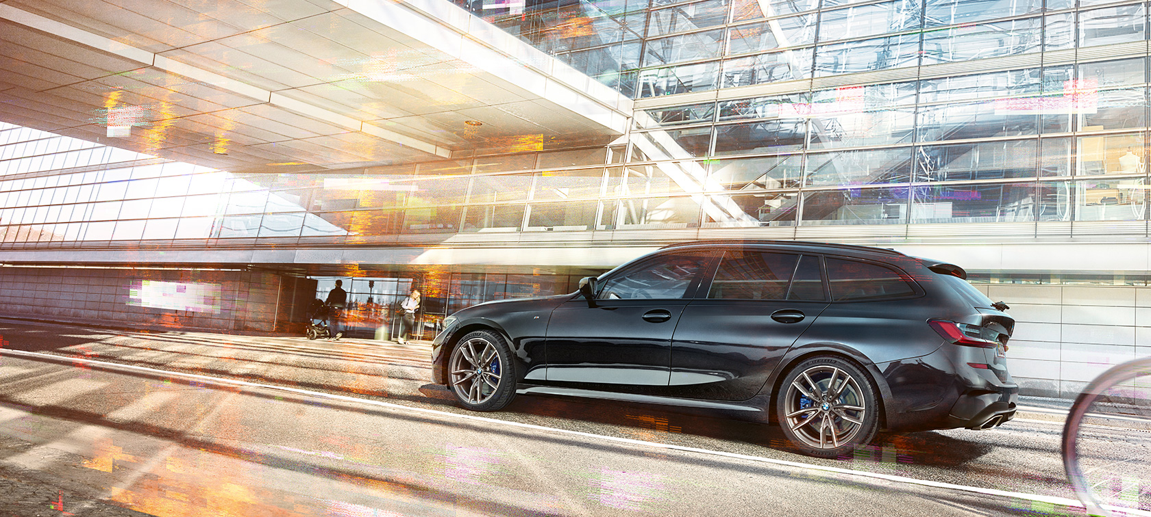 BMW M340i xDrive Touring, šoninis važiuojančio automobillo vaizdas BMW M340i xDrive Touring, šoninis važiuojančio pro stiklinį miesto pastatą automobillo vaizdas iš priekio