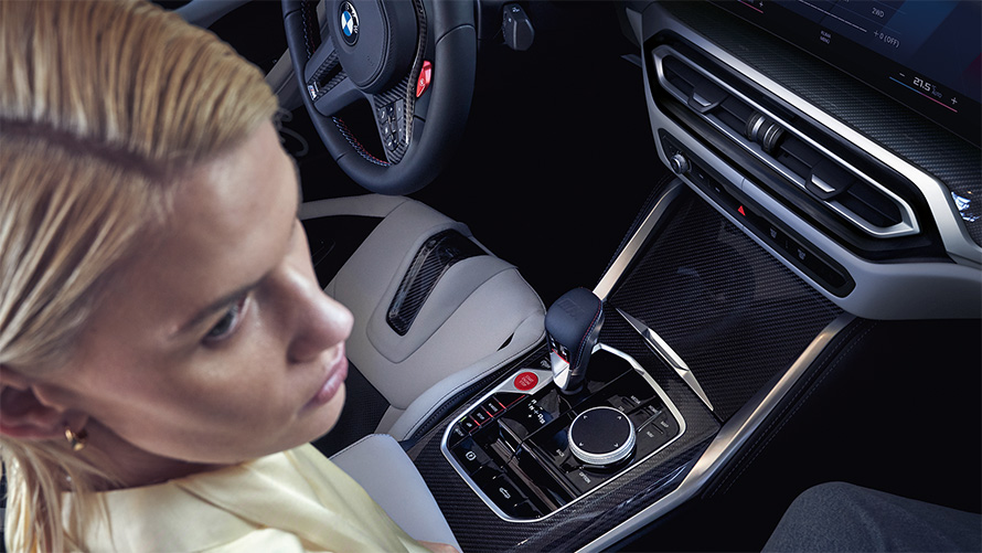 BMW M4 Competition kabrioletas su M xDrive (G83) 2021, centrine konsolė BMW M4 Competition kabrioletas su M xDrive (G83) 2021, centrine konsolė ir moteris keleivio sėdynėje