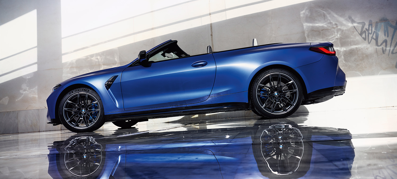 2021 metų BMW M4 Competition kabrioletas su M xDrive (G83), vaizdas iš šono žemu kampu BMW M440i xDrive kabrioletas su M xDrive (G83) 2021 mėlynos BMW Individual Frozen Portimao Blue metalizuotos kėbulo spalvos stovinčio automobilio šoninis vaizdas žemu kampu