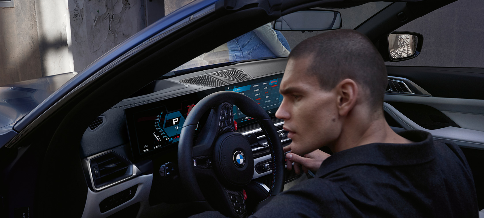 BMW M4 Competition kabrioletas su M xDrive (G83) 2021 vairuotojo erdvė BMW M4 Competition kabrioletas su M xDrive (G83) 2021 mėlynos metalizuotos BMW Individual Frozen Portimao Blue kėbulo spalvos, vairuotojo erdvės vaizdas pro atviras dureles su modeliu