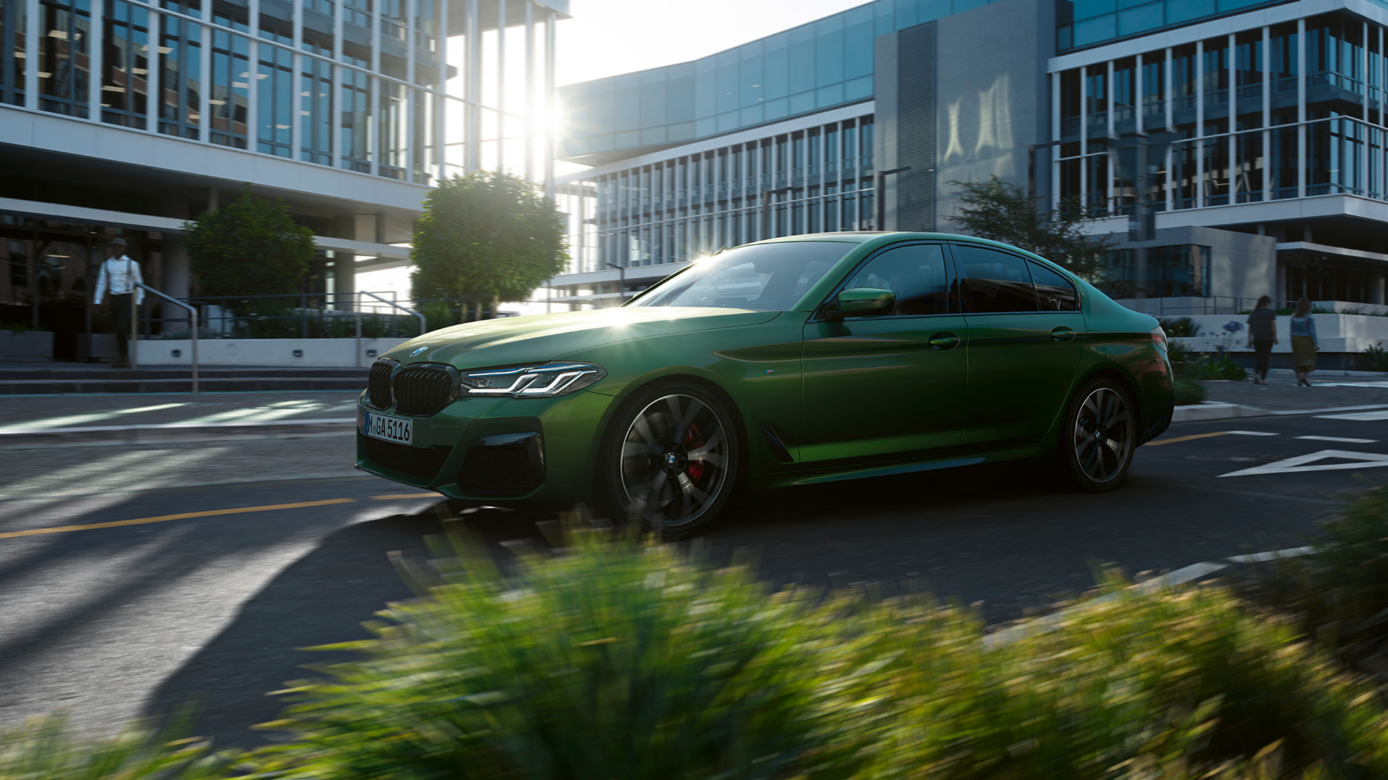 BMW M550i xDrive sedanas G30 LCI Facelift 2020 važiuojančio automobilio vaizdas iš šono BMW M550i xDrive sedanas G30 LCI Facelift 2020, BMW Individual žalio Verde Ermes metaliko spalvos, mieste važiuojančio automobilio vaizdas iš šono