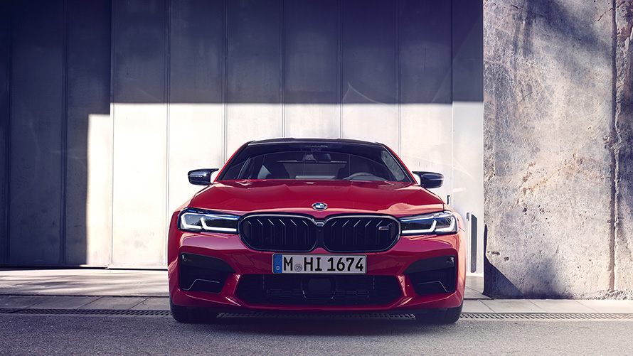BMW M5 Competition F90 LCI Facelift 2020 BMW Individual raudonos „Imola Red“ spalvos vaizdas iš priekio parkingo fone