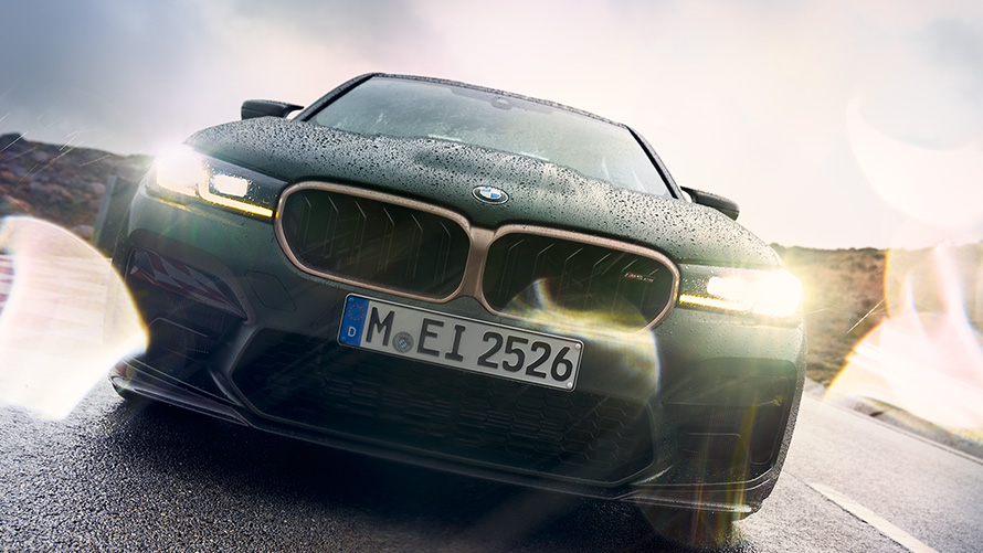 BMW M5 CS F90 2021 žalio „Frozen Deep Green“ metaliko spalvos, įjungtų priekinių žibintų vaizdas iš priekio