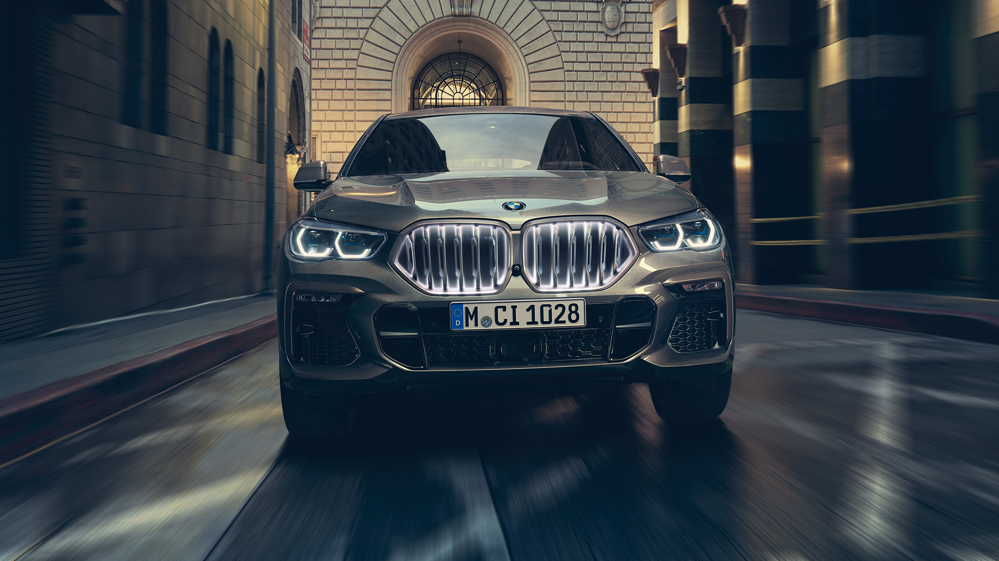 BMW X6 M50i su BMW priekinėmis grotelėmis Iconic Glow BMW X6 M50i trijų ketvirčių vaizdas iš priekio miesto fone