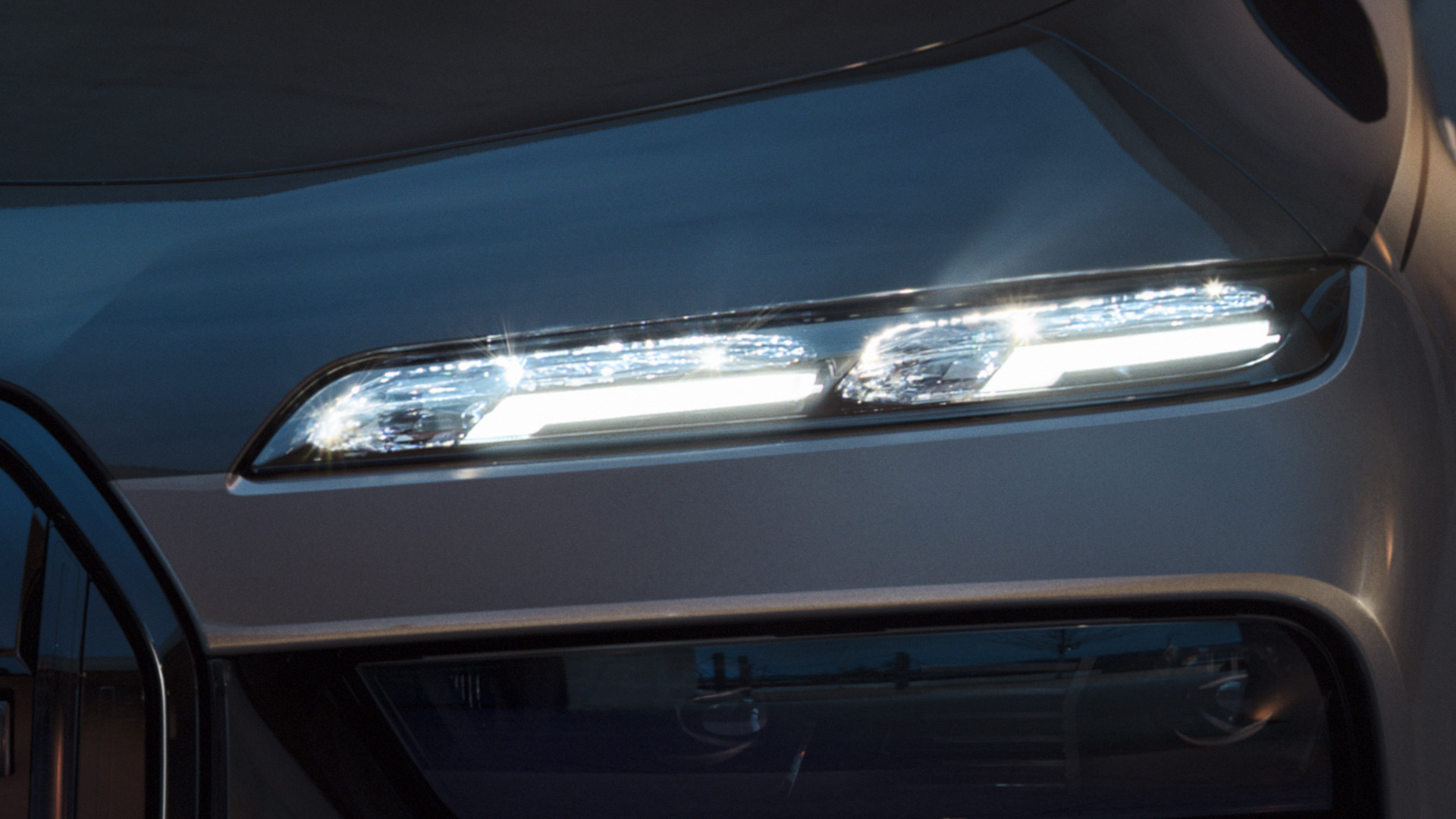 BMW krištolo priekiniai žibintai Iconic Glow BMW M760e xDrive sedanas G70 BMW krištolo priekiniai žibintai Iconic Glow BMW M760e xDrive sedanas G70 BMW Individual dviejų atspalvių Black Sapphire juoda metalizuota dažų apdaila BMW Individual Dravite Grey pilka metalizuota spalva, vaizdas su įjungtomis šviesomis iš arti