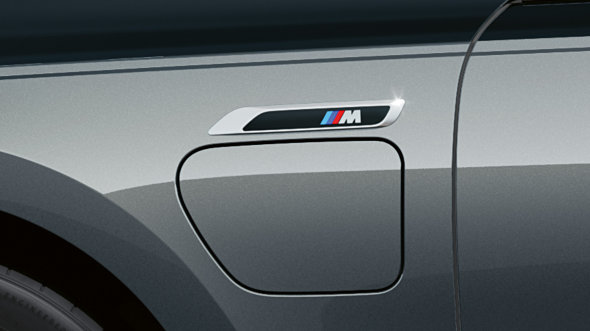 M ženklelis BMW M760e xDrive sedanas G70 M ženklelis BMW M760e xDrive sedanas G70 M Performance paketas BMW Individual dviejų atspalvių Black Sapphire juoda metalizuota dažų apdaila BMW Individual Dravite Grey pilka metalizuota spalva priartintas vaizdas iš šono