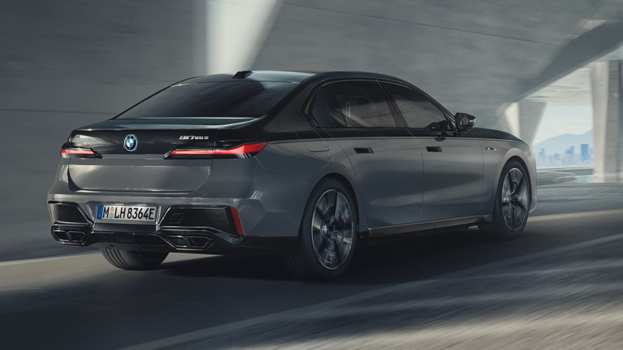 BMW M760e xDrive sedanas G70 M Performance paketas BMW M760e xDrive sedanas G70 M Performance paketas BMW Individual dviejų atspalvių Black Sapphire juoda metalizuota dažų apdaila BMW Individual Dravite Grey pilkos metalizuotos spalvos važiuojančio gatve automobilio trijų ketvirčių vaizdas iš galo