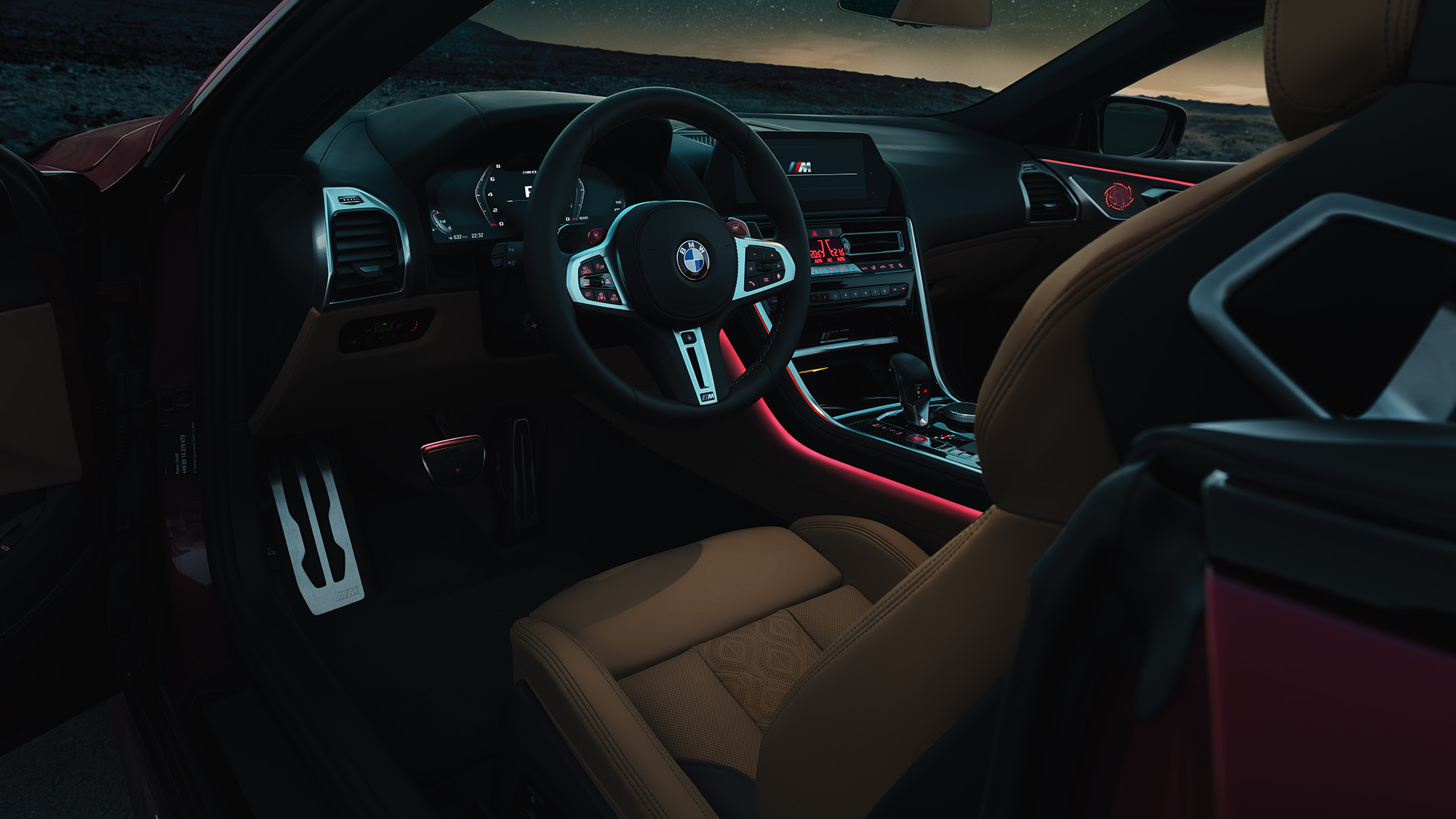 BMW M8 Competition kabrioletas, vairuotojo erdvė. BMW M8 Competition kabrioletas, vairuotojo erdvės su M odiniu vairu ir raudonu apšvietimu vaizdas naktį.