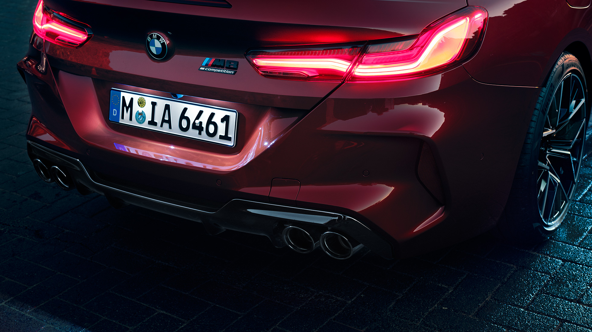 BMW M8 Competition kabrioletas, priartintas vaizdas iš galo. BMW M8 Competition kabrioletas Motegi Red raudono metaliko spalvos, priartintas LED galinių žibintų ir M8 Competiton ženklelio vaizdas iš arti.