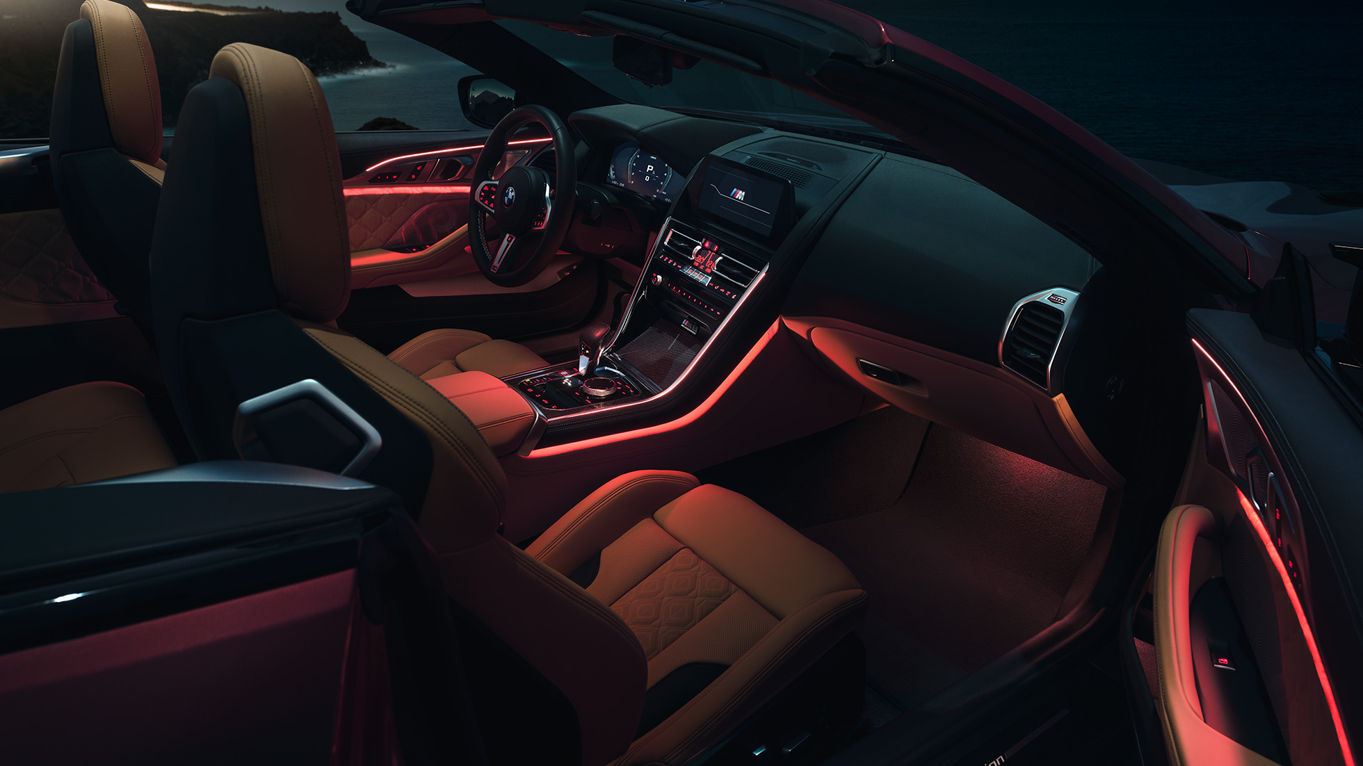 BMW M8 Competition kabrioletas, interjeras. BMW M8 Competition kabrioletas su atviru minkštu stogu, interjeras su raudonu aplinkos apšvietimu naktį.