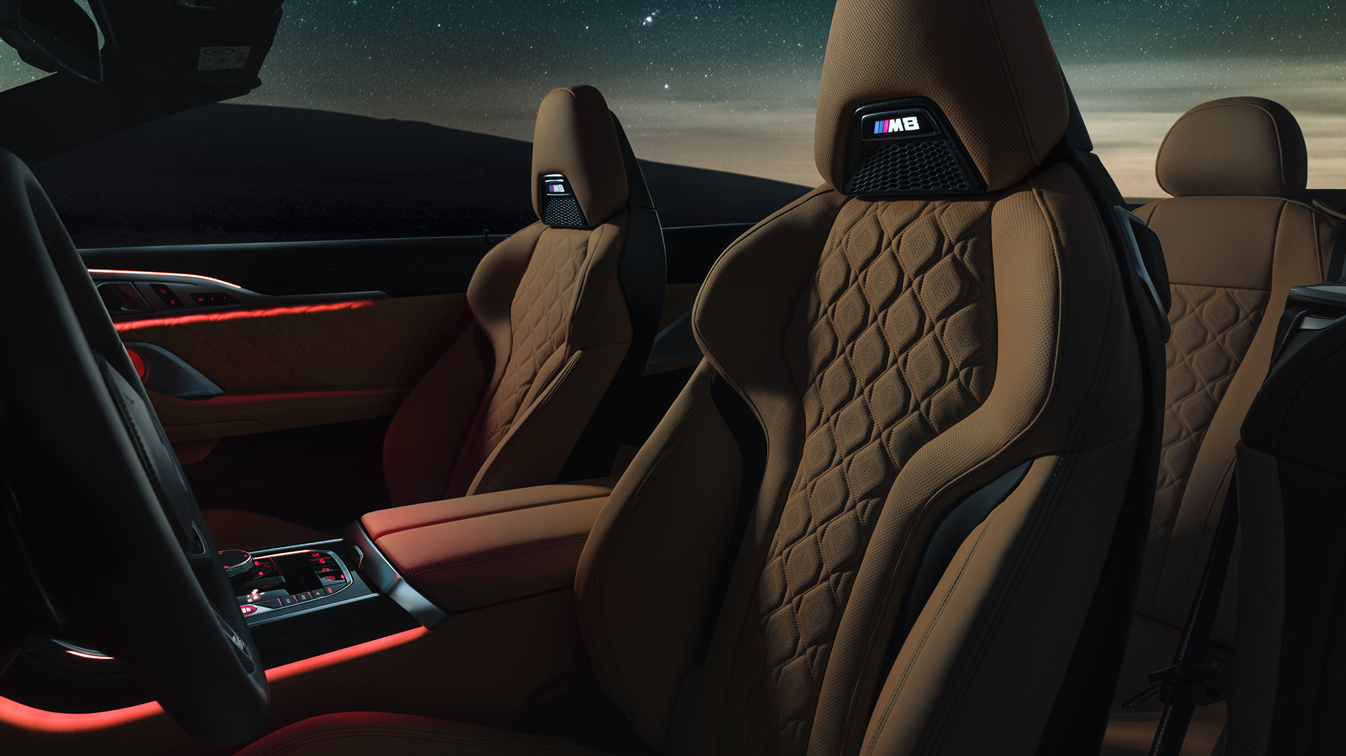 Merino odos M sportinės sėdynės. BMW M8 Competition kabrioletas su atviru minkštu stogu po žvaigždėtu dangumi, interjeras su M sportinėmis Merino odos sėdynėmis ir raudonu aplinkos apšvietimu.