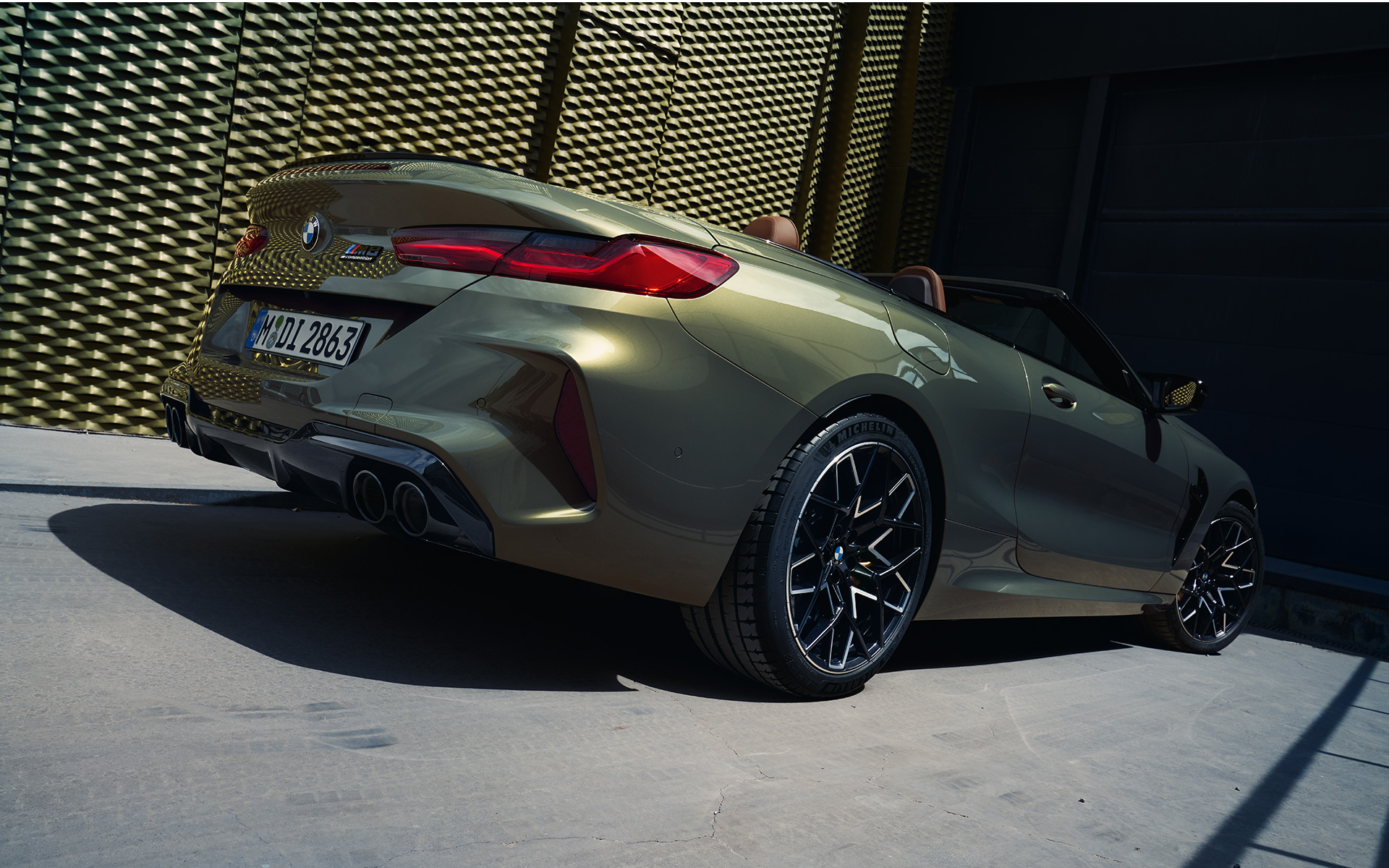 Vaizdas iš šono ant pakylos BMW M8 Competition kabrioletas F91 Facelift 2022 BMW M8 Competition kabrioletas F91 LCI Facelift 2022 BMW Individual Brass metalizuotos spalvos trijų ketvirčių vaizdas iš galo žemu kampu