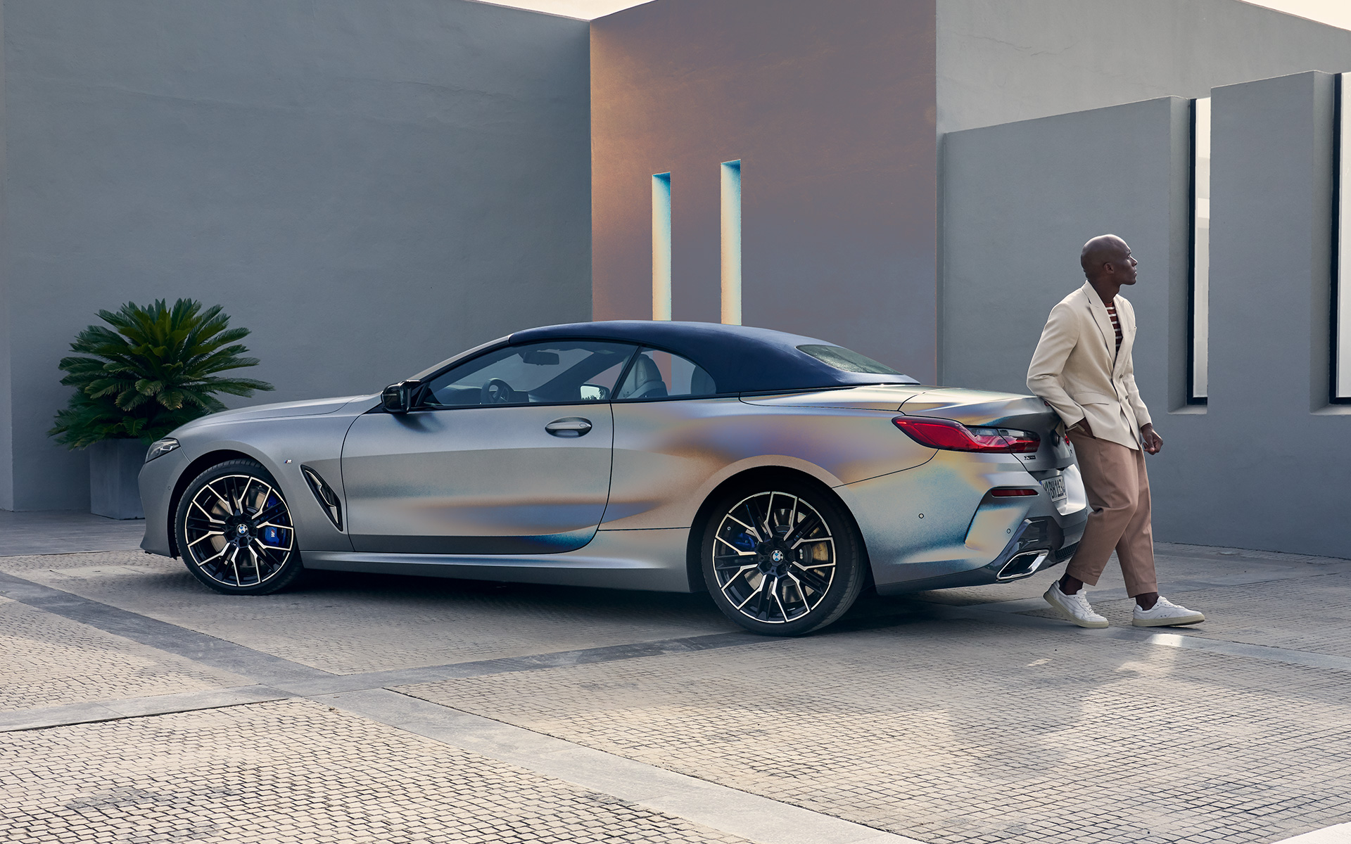 Trijų ketvirčių vaizdas iš galo BMW M850i xDrive kabrioletas G14 LCI Facelift 2022 BMW M850i xDrive kabrioletas G14 LCI Facelift 2022 BMW Individual pilkos Frozen Pure Grey metalizuotos spalvos trijų ketvirčių vaizdas iš galo su modeliu šalia automobilio