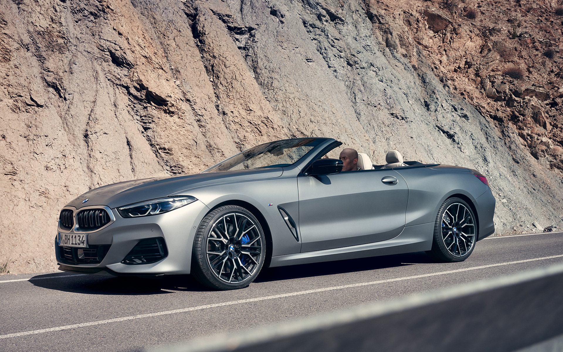 Trijų ketvirčių vaizdas iš priekio BMW M850i xDrive kabrioletas G14 LCI Facelift 2022 BMW M850i xDrive kabrioletas G14 LCI Facelift 2022 BMW Individual pilkos Frozen Pure Grey metalizuotos spalvos uolos fone važiuojančio automobilio trijų ketvirčių vaizdas iš priekio
