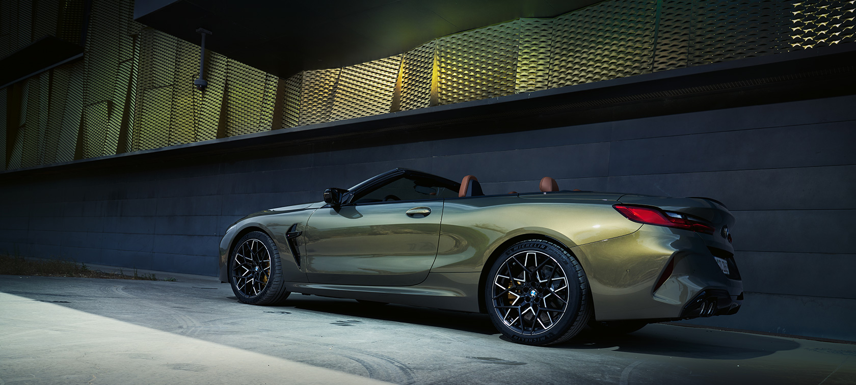 BMW M8 Competition kabrioletas F91 LCI Facelift 2022 BMW Individual Brass metalizuotos kėbulo spalvos sienos fone stovinčio automobilio trijų ketvirčių vaizdas iš šono