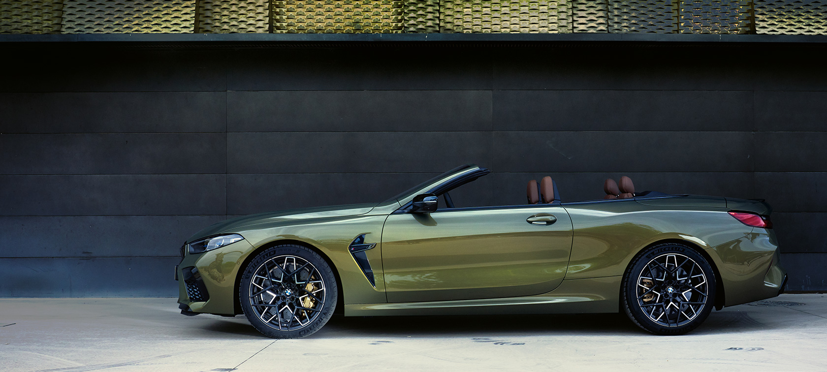 BMW M8 Competition kabrioletas F91 LCI Facelift 2022 stovinčio automobilio vaizdas iš šono BMW M8 Competition kabrioletas F91 LCI Facelift 2022 BMW Individual metalizuotos Brass spalvos, automobilio atviromis durelėmis vaizdas iš šono su moterimi šalia