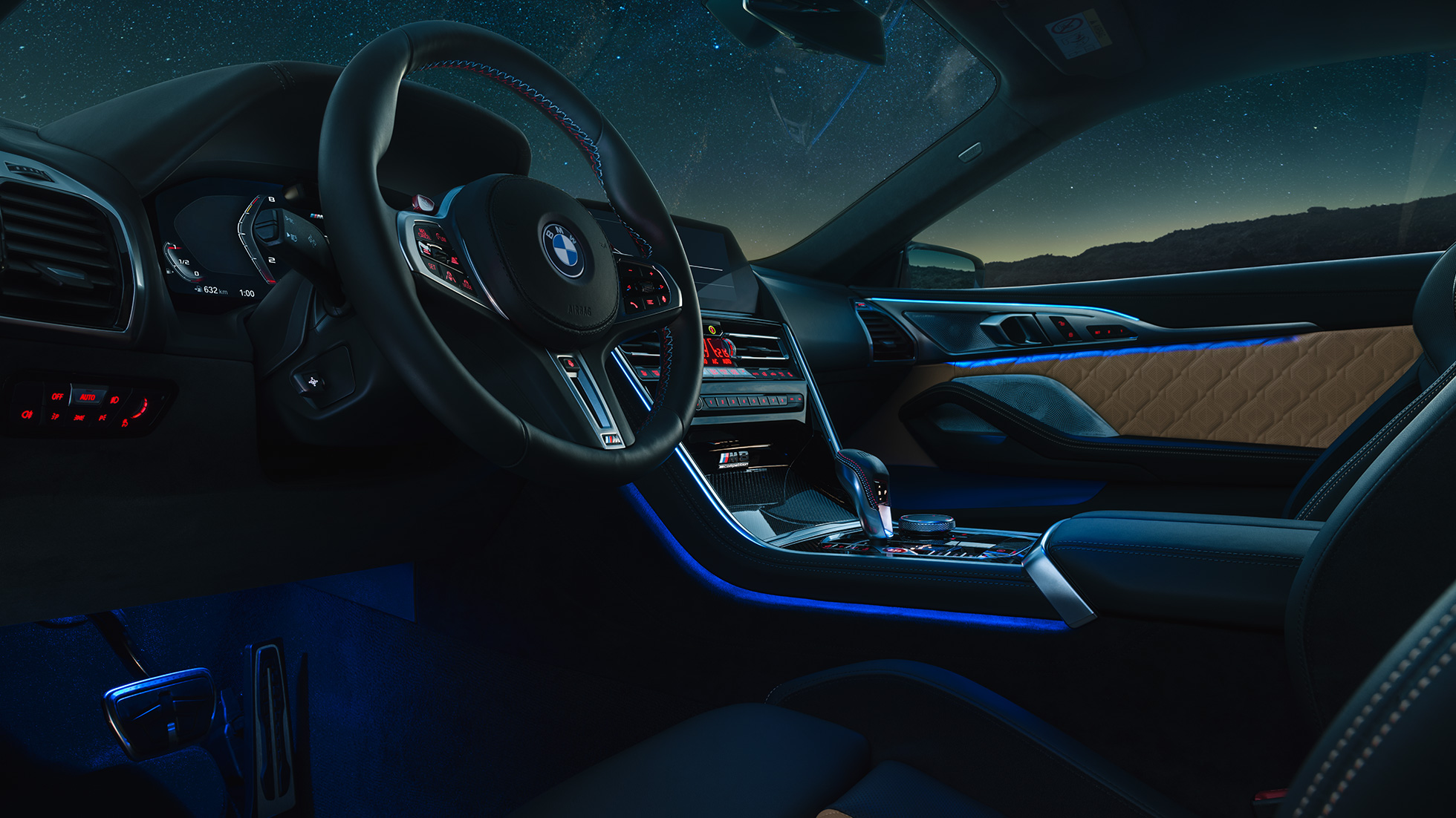 BMW M8 Competition kupė vairuotojo ervdė BMW M8 Competition kupė, vairuotojo erdvės su M odiniu vairu ir mėlynu apšvietimu vaizdas naktį