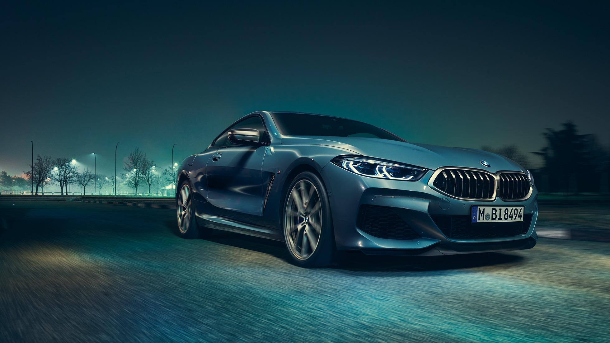 BMW M850i xDrive kupė, trijų ketvirčių vaizdas iš kairės priekinės pusės BMW M850i xDrive kupė Barcelona Blue mėlyno metaliko spalvos, trijų ketvirčių naktį važiuojančio automobilio vaizdas iš kairės priekinės pusės