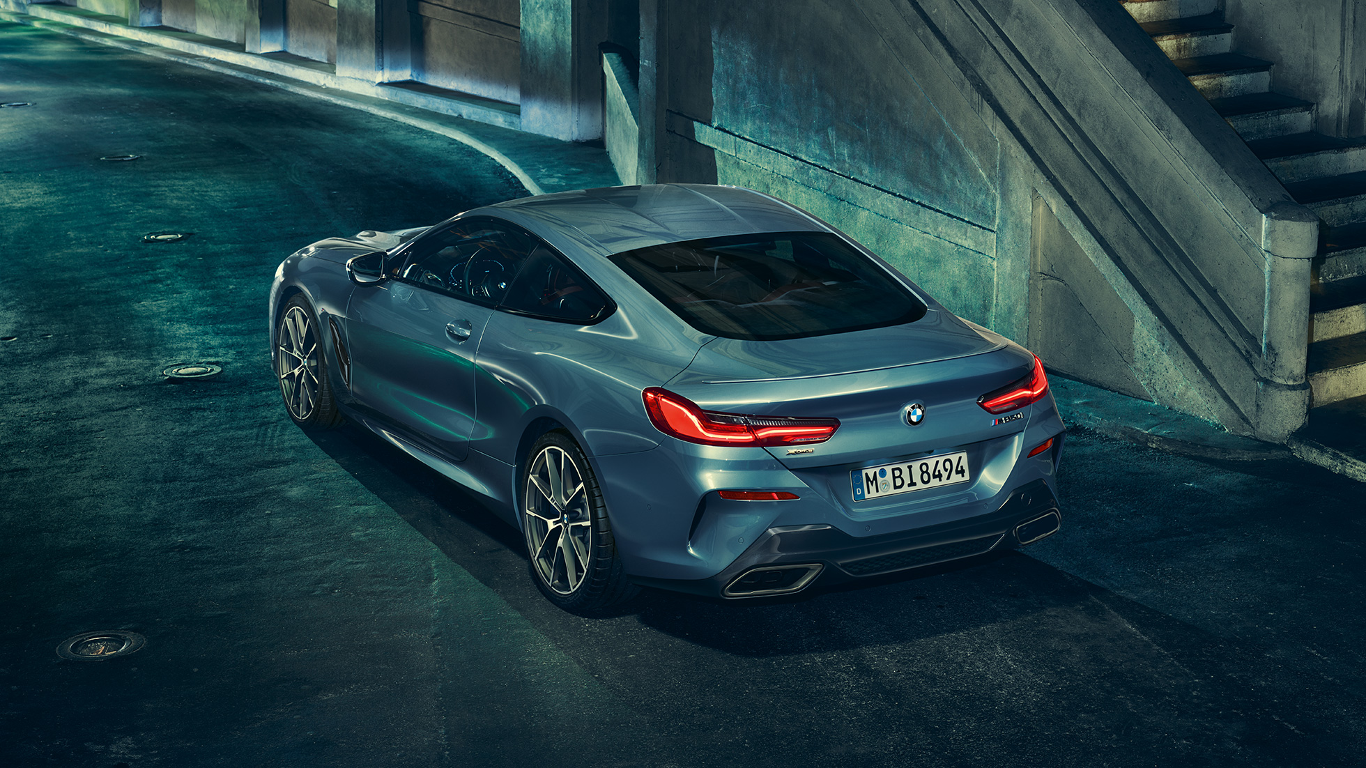 BMW M850i xDrive kupė, trijų ketvirčių vaizdas iš galinės kairės pusės BMW M850i xDrive kupė Barcelona Blue mėlyno metaliko spalvos, trijų ketvirčių naktį stovinčio automobilio vaizdas iš galinės kairės pusės