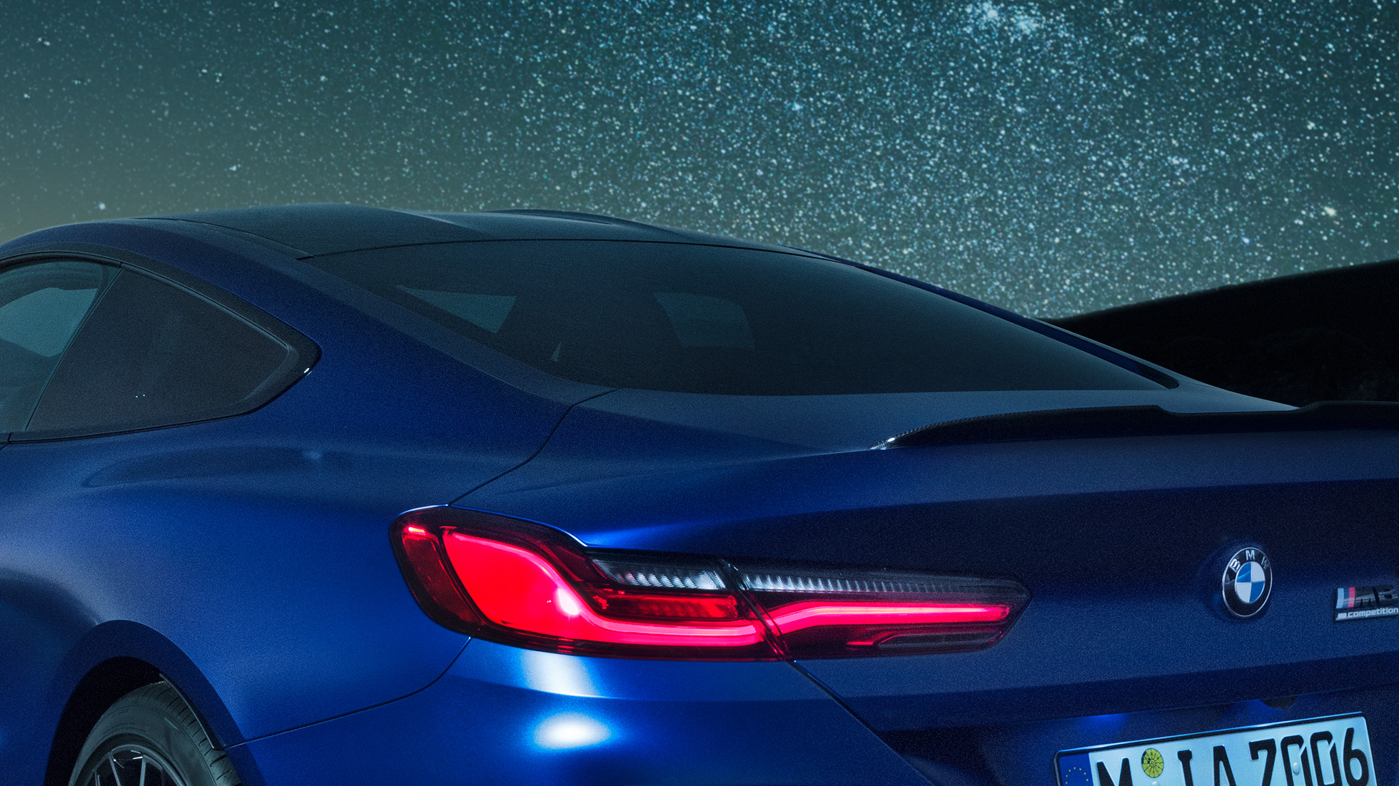M galinis aptakas BMW M8 Competition kupė Marina Bay Blue mėlyno metaliko spalvos, M Carbon galinio aptako vaizdas naktį iš arti