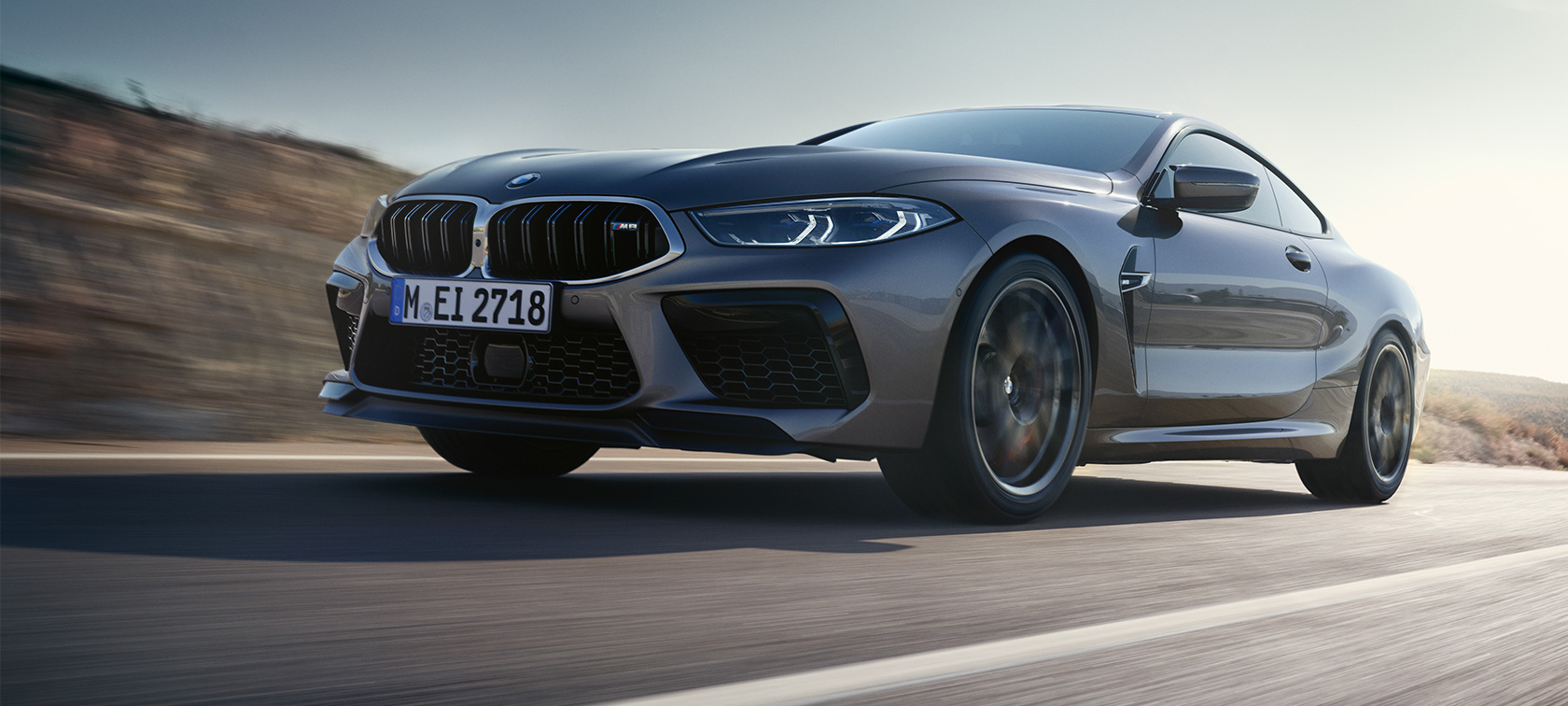 BMW M8 kupė F92 LCI Facelift 2022 važiuojančio automobilio trijų ketvirčių vaizdas iš šono BMW M8 kupė F92 LCI Facelift 2022 pilkos Skyscraper Grey kėbulo spalvos trijų ketvirčių vaizdas iš šono žemu kampu