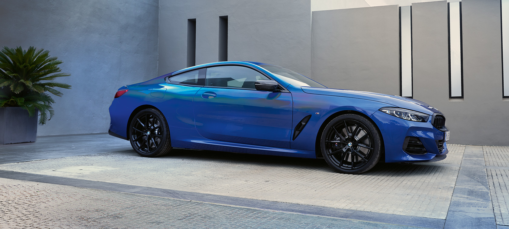 Vaizdas iš šono BMW M850i xDrive kupė G15 LCI Facelift 2022 BMW M850i xDrive kupė G15 LCI 2022 Facelift mėlynos metalizuotos M Portimao Blue kėbulo spalvos pastato fone stovinčio automobilio vaizdas iš šono