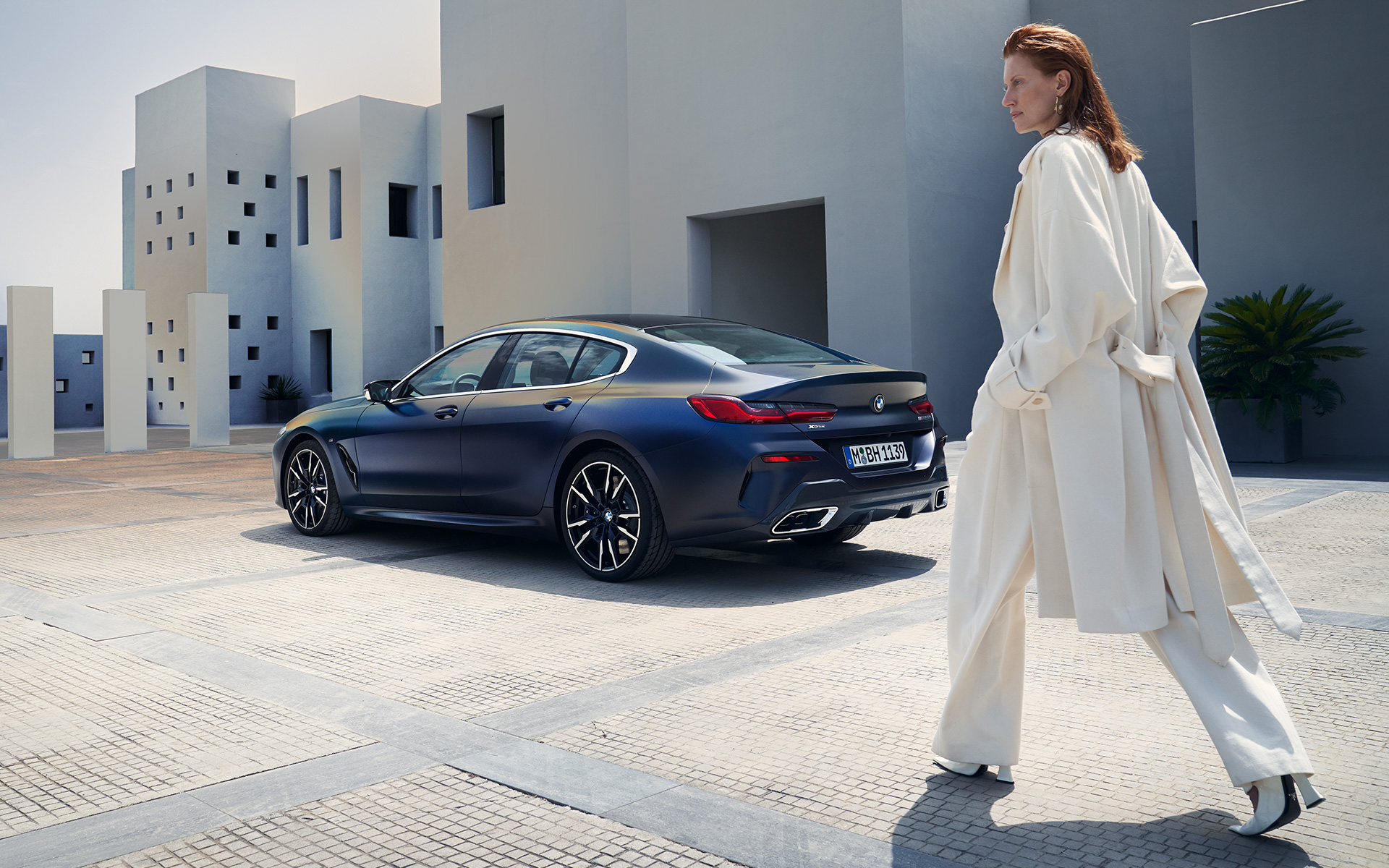 BMW M850i xDrive Gran kupė G16 LCI Facelift 2022 vaizdas iš šono su moterimi modeliu BMW M850i xDrive Gran kupė G16 LCI Facelift 2022 BMW Individual metalizuotos Frozen Tanzanite Blue mėlynos kėbulo spalvos trijų ketvirčių vaizdas iš galo su moterimi modeliu