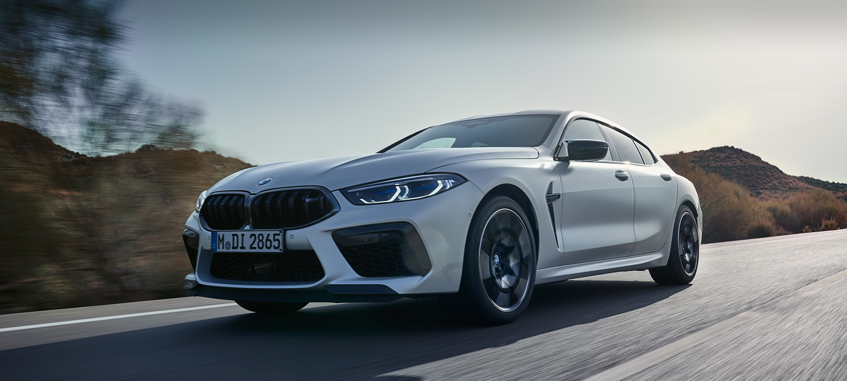 BMW M8 Competition Gran kupė F93 LCI Facelift 2022 BMW Individual metalizuotos Frozen Brilliant White baltos kėbulo spalvos važiuojančio automobilio trijų ketvirčių vaizdas iš priekio