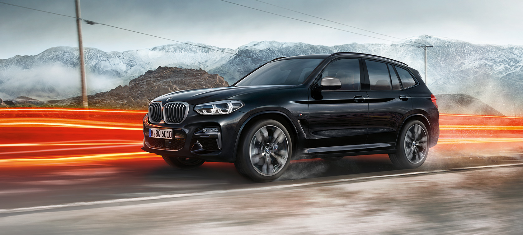 BMW X3 M40i ir BMW X3 M40d, vaizdas iš šono. BMW X3 M40i ir BMW X3 M40d „Black Sapphire“ juodo metaliko spalvos, važiuojantis keliu, eksterjeras, vaizdas apšviestų kalnų fone.