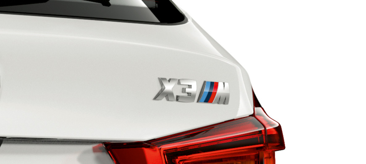 BMW X3 M, modelio ženklelis. BMW X3 M „Alpine White“ baltos spalvos, eksterjeras, galinė dalis su modelio ženkleliu.
