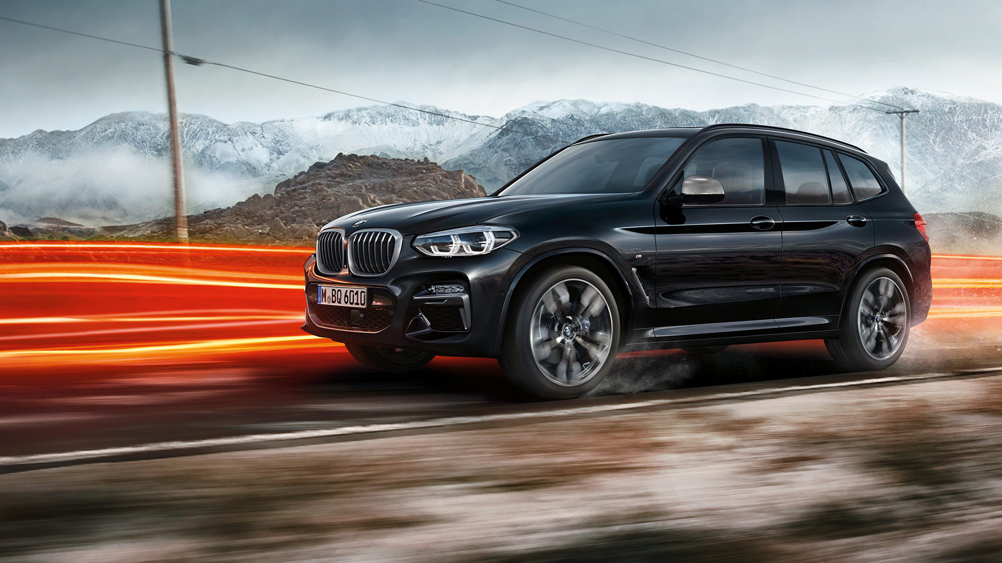 BMW X3 M40i ir BMW X3 M40d, vaizdas iš šono. BMW X3 M40i ir BMW X3 M40d „Black Sapphire“ juodo metaliko spalvos, važiuojantys keliu, eksterjeras, vaizdas iš šono apšviestų kalnų fone.