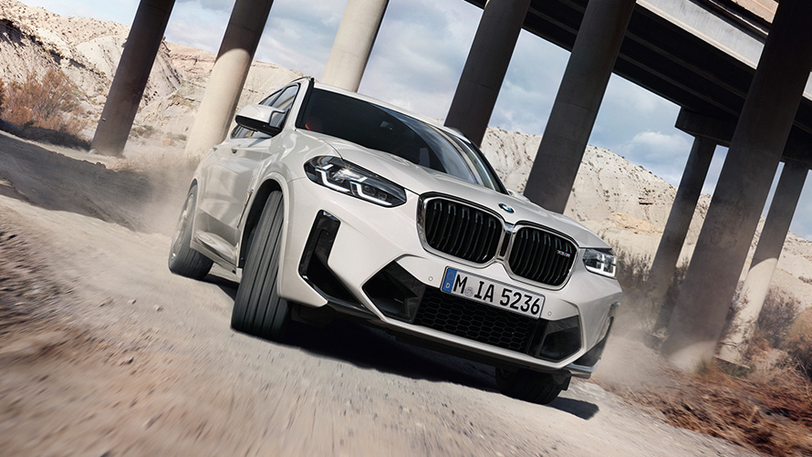 BMW X3 M (F97) LCI Facelift 2021 trijų ketvirčių vaizdas iš priekio įveikiant posūkį BMW X3 M (F97) LCI Facelift 2021 baltos Alpine White kėbulo spalvos, trijų ketvirčių vaizdas iš priekio įveikiant posūkį