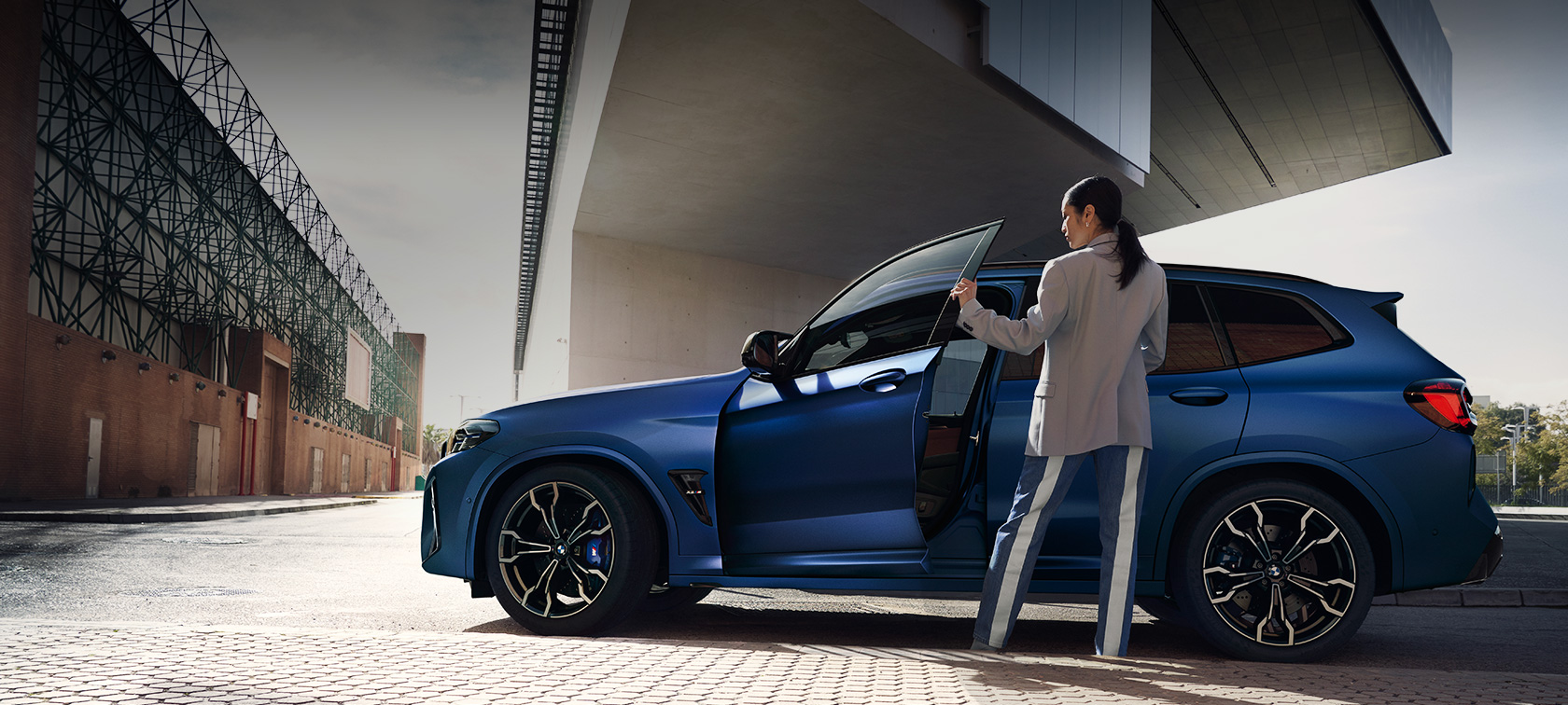 BMW X3 Competition F97 LCI Facelift 2021 vaizdas iš šono BMW X3 M Competition F97 LCI Facelift 2021 BMW Individual metalizuotos mėlynos BMW Frozen Portimao Blue spalvos, automobilio atviromis durelėmis vaizdas iš šono su moterimi šalia