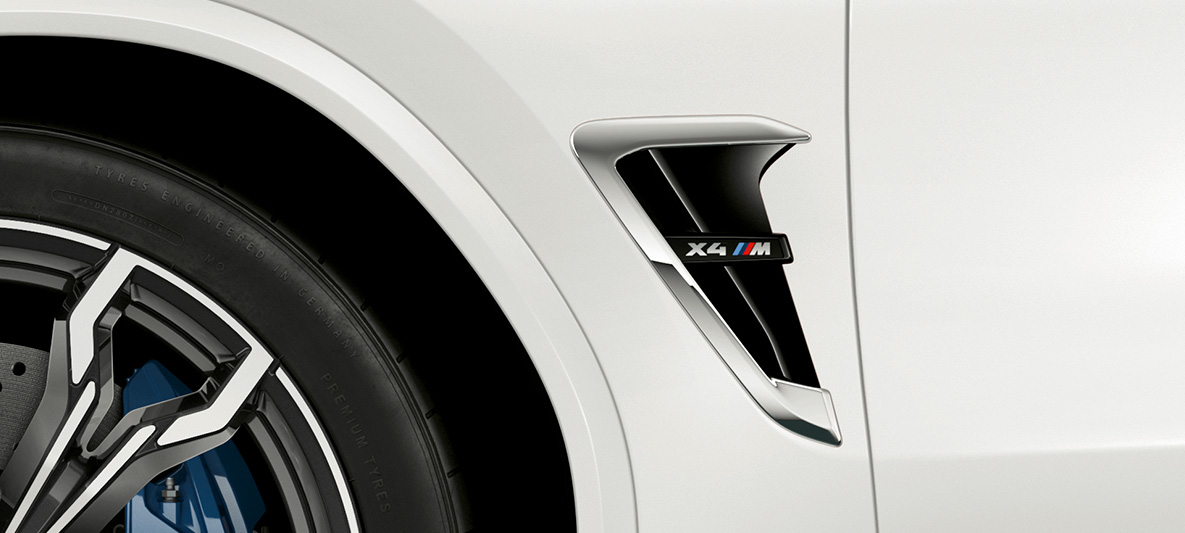 BMW X4 M, M šoninė oro anga. BMW X4 M „Alpine White“ baltos spalvos, eksterjeras, M šoninės oro angos su chromo akcentais ir modelio ženkleliu.