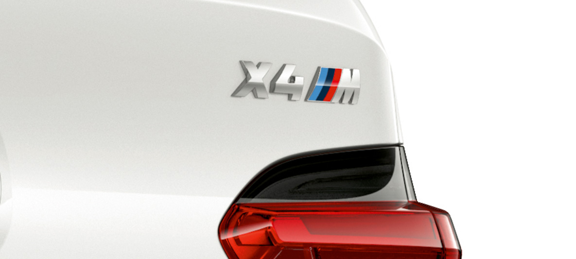 BMW X4 M, modelio ženklelis. BMW X4 M „Alpine White“ baltos spalvos, eksterjeras, galinė dalis su modelio ženkleliu stambiu planu.