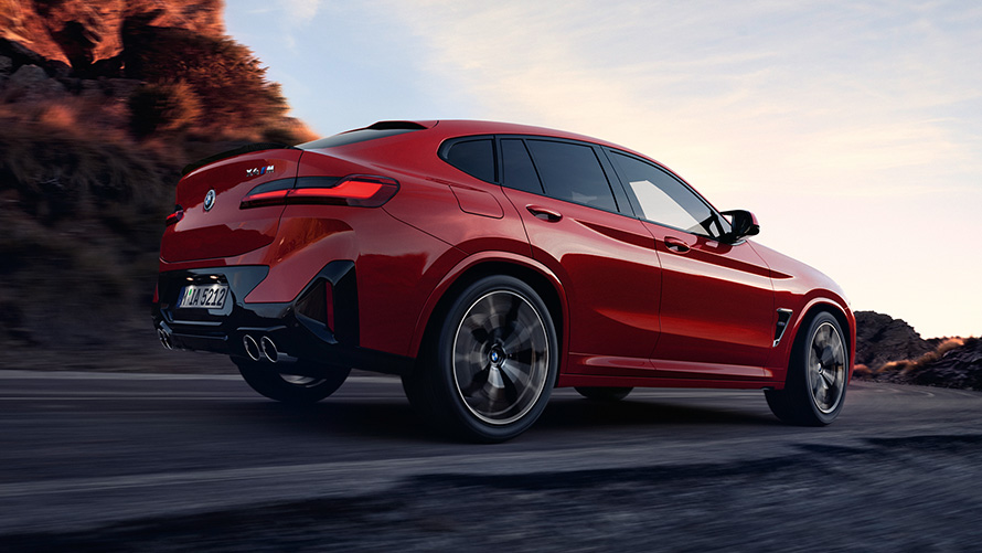 BMW X4 M (F98) LCI Facelift 2021 raudonos metalizuotos Toronto Red kėbulo spalvos keliu važiuojančio automobilio trijų ketvirčių vaizdas iš galo