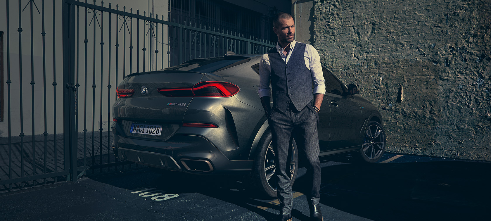 BMW X6 M50i trijų ketvirčių vaizdas iš galo (G06) Šalia BMW X6 M50i (G06) 2018 stovintis vyras, SUV trijų ketvirčių vaizdas iš galo