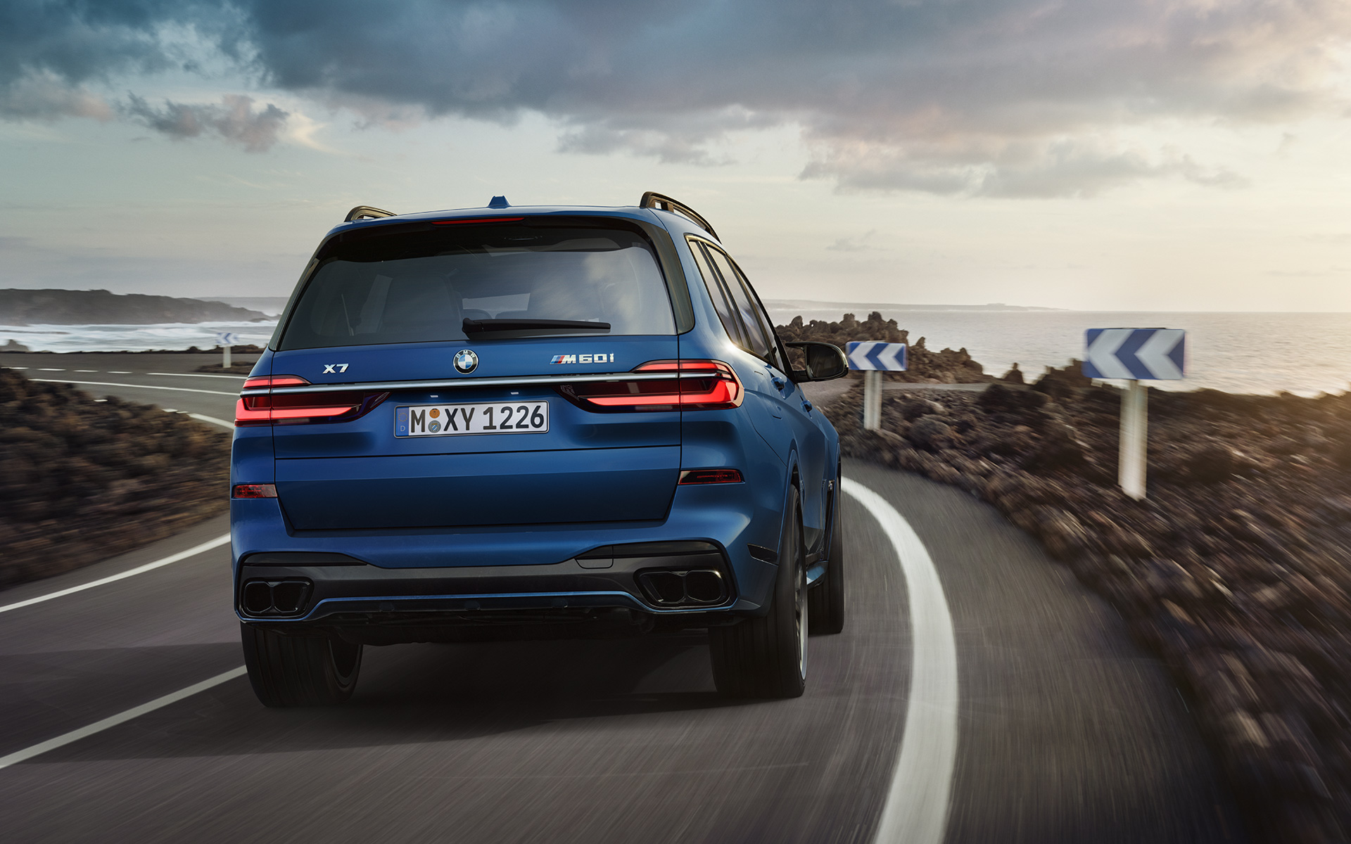 BMW X7 M60i G07 LCI mėlynos Frozen Marina Bay Blue kėbulo spalvos važiuojančio automobilio vaizdas iš galo BMW X7 M60i G07 LCI mėlynos Frozen Marina Bay Blue kėbulo spalvos važiuojančio automobilio vaizdas iš galo