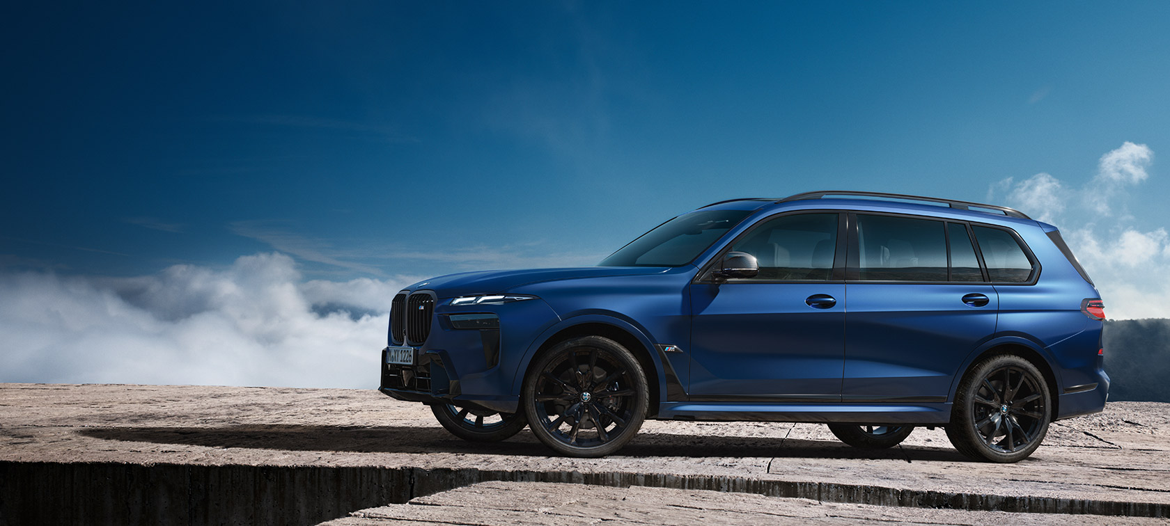 BWM X7 M60i xDrive G07 LCI mėlynos Frozen Marina Bay Blue kėbulo spalvos stovinčio automobilio vaizdas iš šono kalnų fone