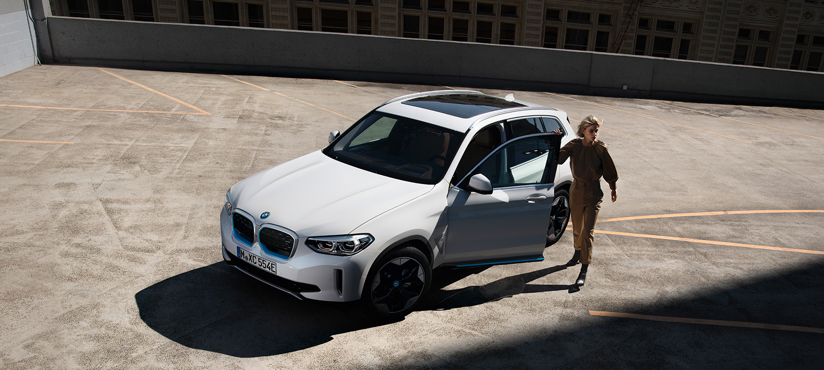BMW iX3 G08 2020 balto Mineral White metaliko spalvos, trijų ketvirčių vaizdas iš priekio su moterimi miesto fone