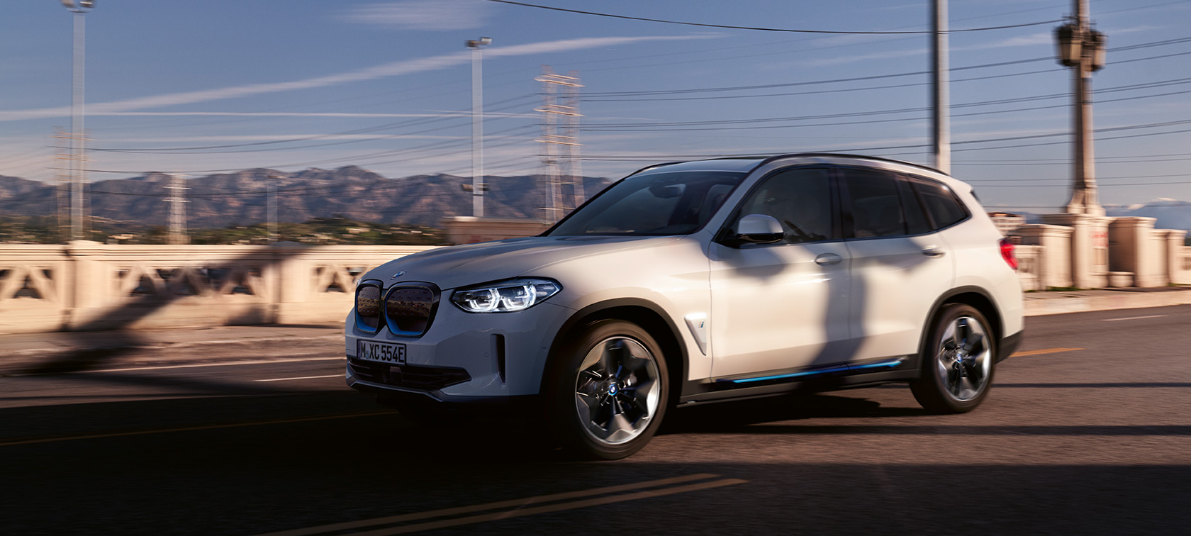 Keliu važiuojančio BMW iX3 G08 trijų ketvirčių vaizdas iš priekio BMW iX3 G08 2020 balto Mineral White metaliko spalvos keliu važiuojančio automobilio trijų ketvirčių vaizdas iš priekio