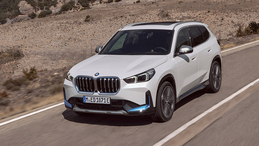 BMW iX1 U11 pirmoji karta, keliu važiuojančio automobilio trijų ketvirčių vaizdas iš priekio BMW X serija BMW iX1 U11 pirmoji karta, keliu važiuojančio automobilio trijų ketvirčių vaizdas iš priekio